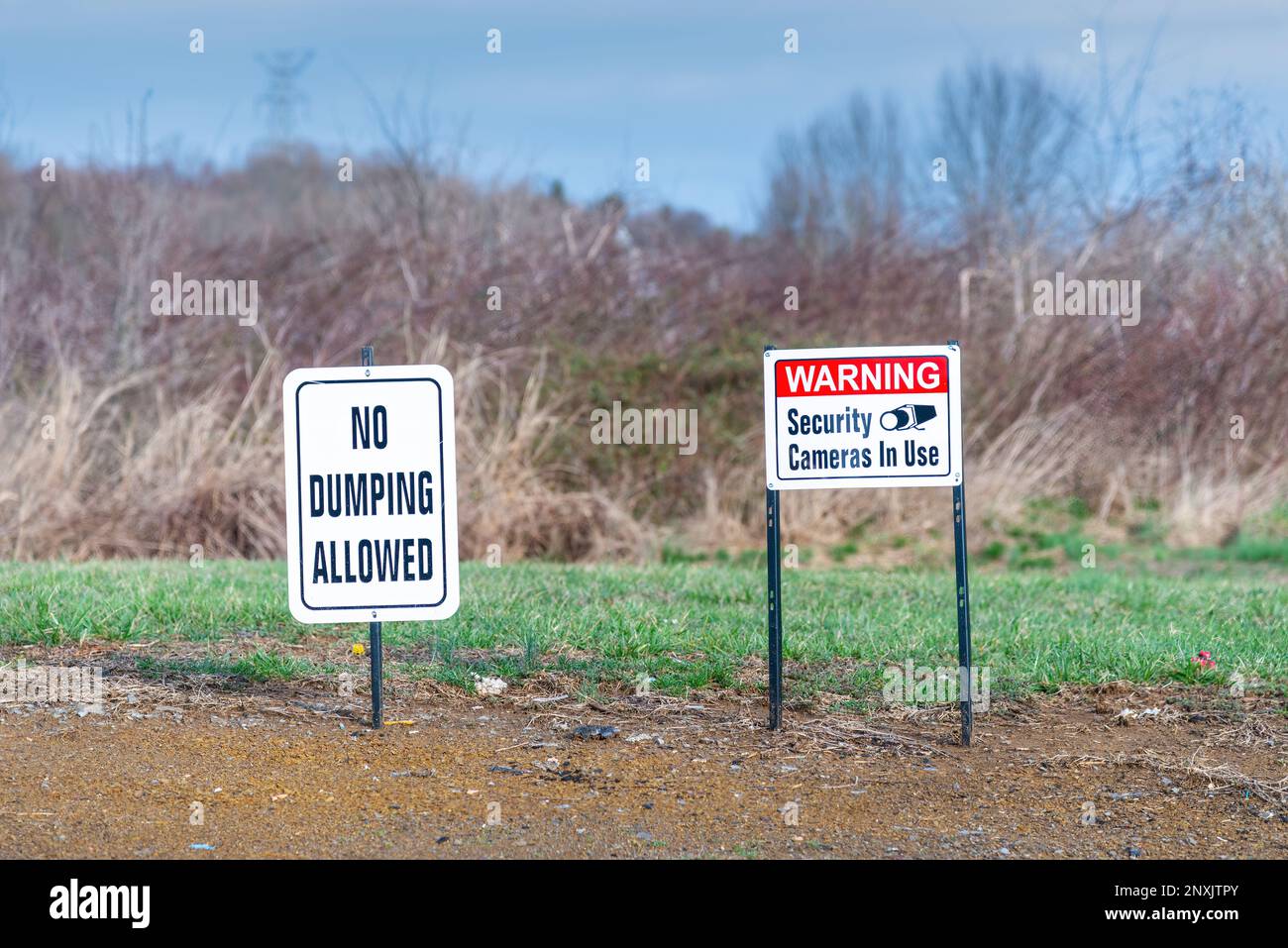 Horizontal shot of a No Dumping Allowed sign and a Warning Security Cameras In Use sign in a field. Stock Photo