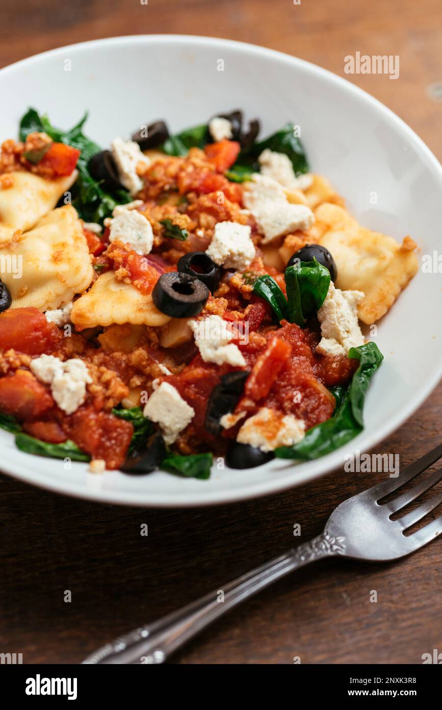 Bowl with vegan ravioli with spinach, TVP, olives, a tomato sauce and ...