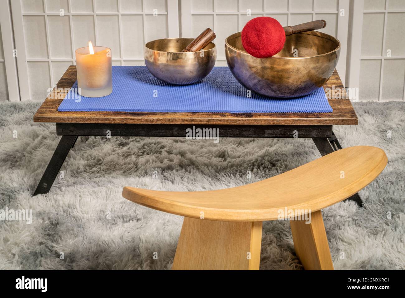large Tibetan singing bowl with a mallet, roller and wax candle on a low table, and kneeling bench, sound healing and meditation concept Stock Photo