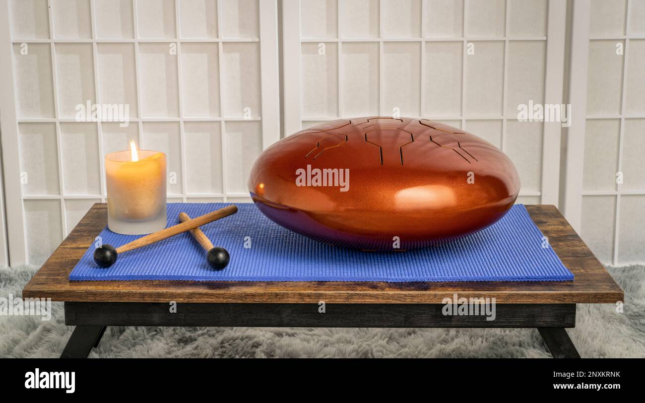 steel tongue drum with mallets and candle on a low table, sound healing and meditation concept