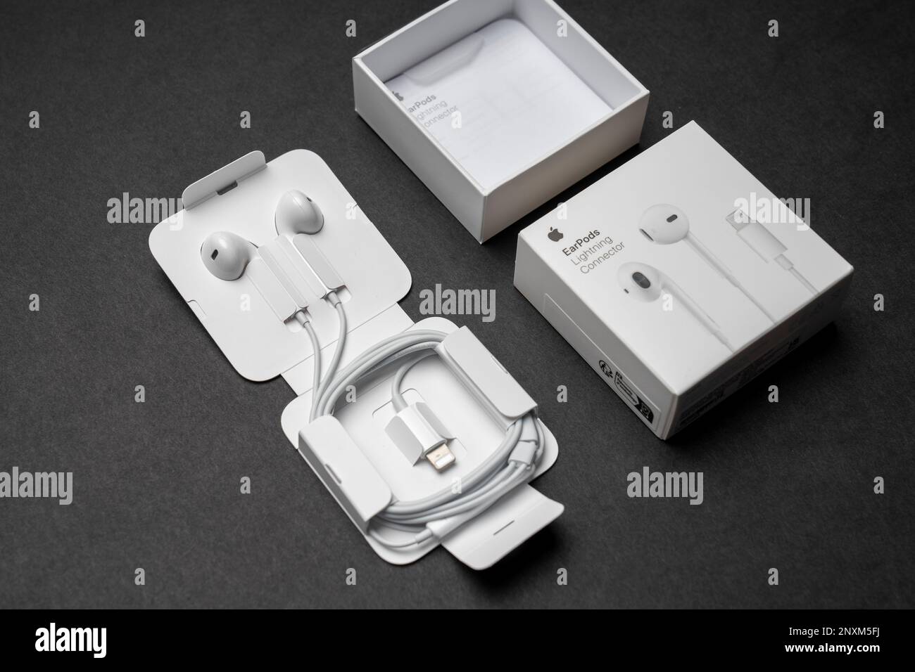 New Apple Earpods, Airpods white earphones for listening to music and podcasts in an open box. Isolated black background. Stock Photo