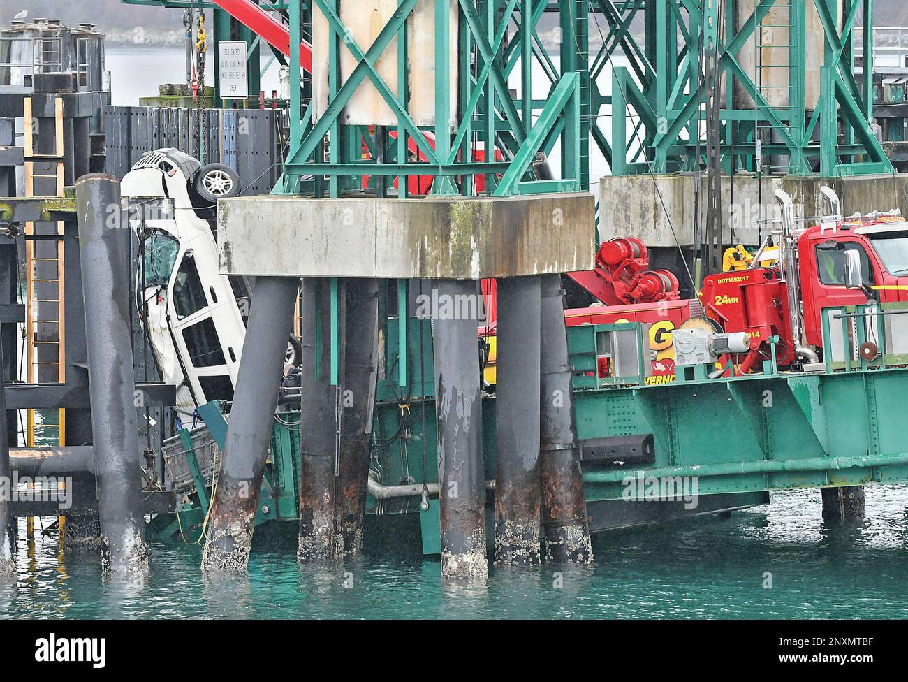 A tow truck lifts a white Jeep Cherokee vehicle out of the water at the