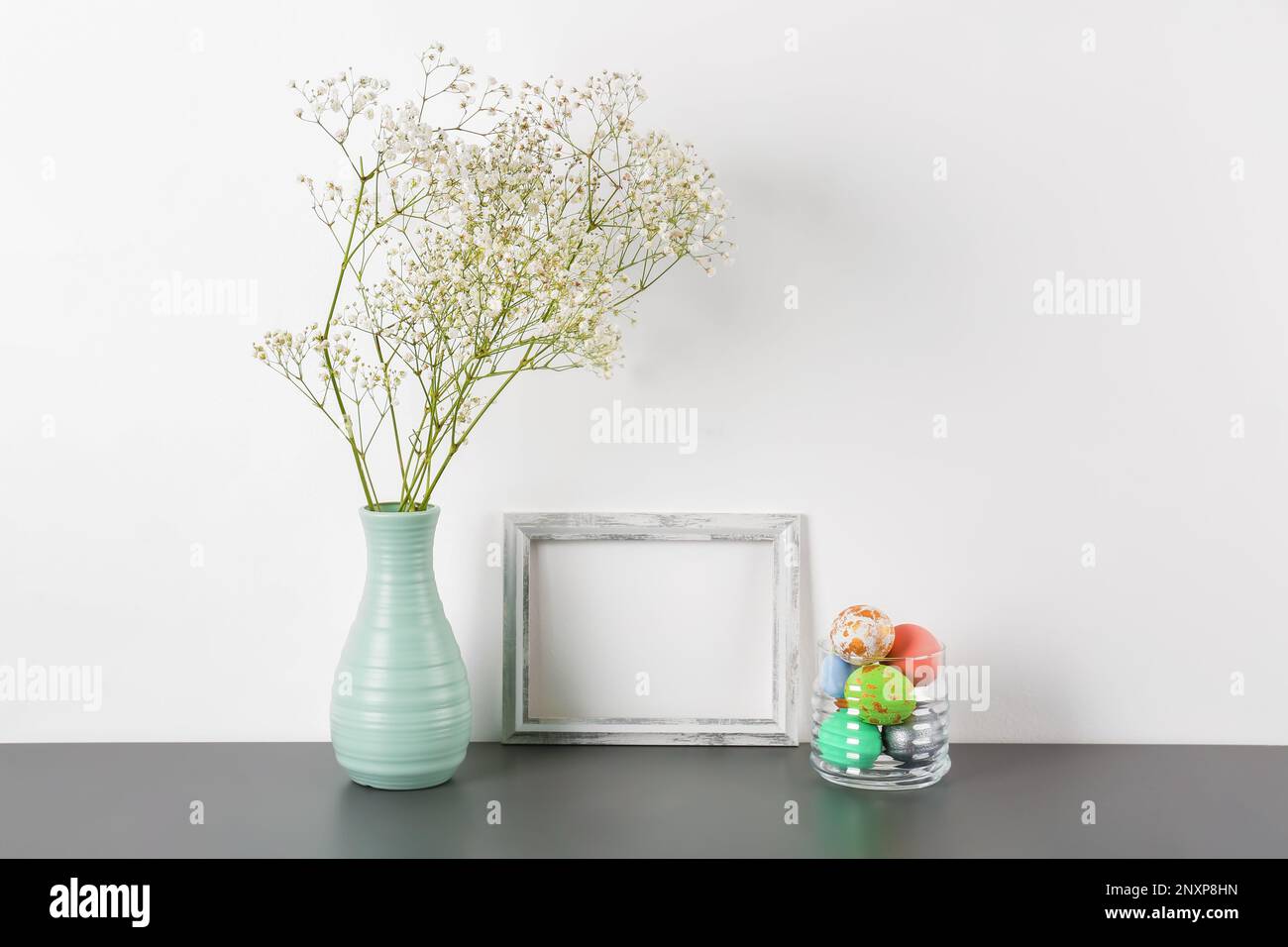 Blank frame, vase with gypsophila flowers and Easter eggs on white ...