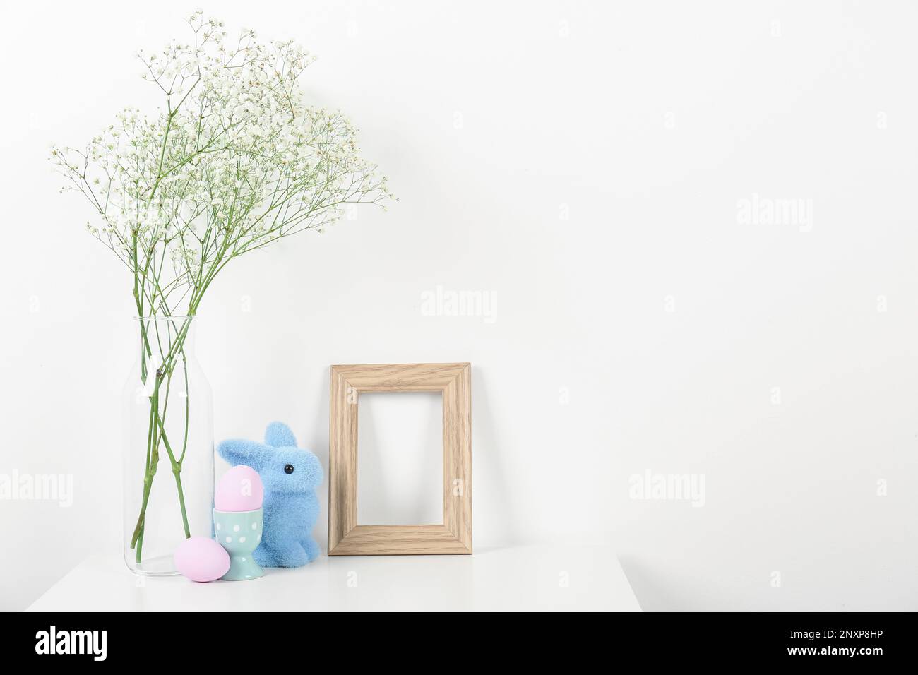 Blank frame, vase with gypsophila flowers, Easter eggs and bunny on ...