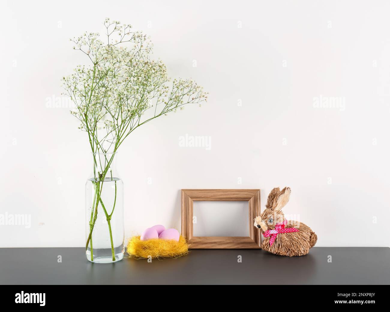Blank frame, vase with flowers, Easter eggs and rabbit on table near ...