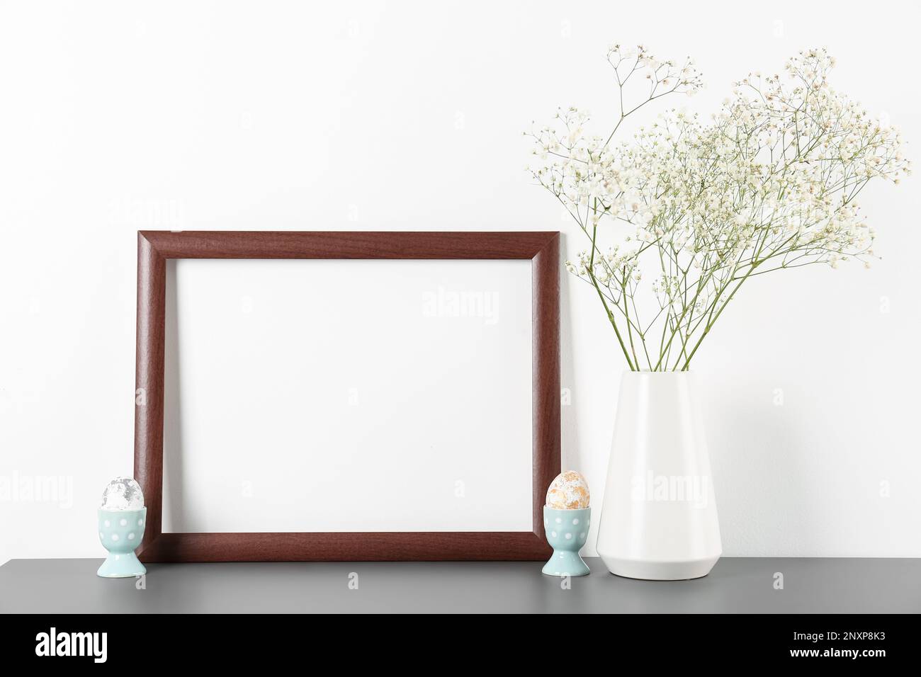 Blank frame, vase with gypsophila flowers and Easter eggs on white ...