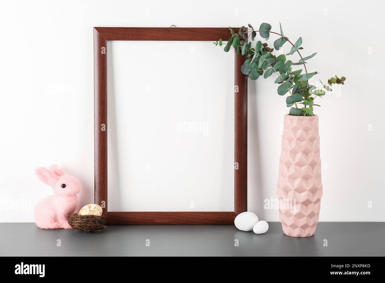 Blank frame, vase with eucalyptus, Easter eggs and rabbit on table near ...