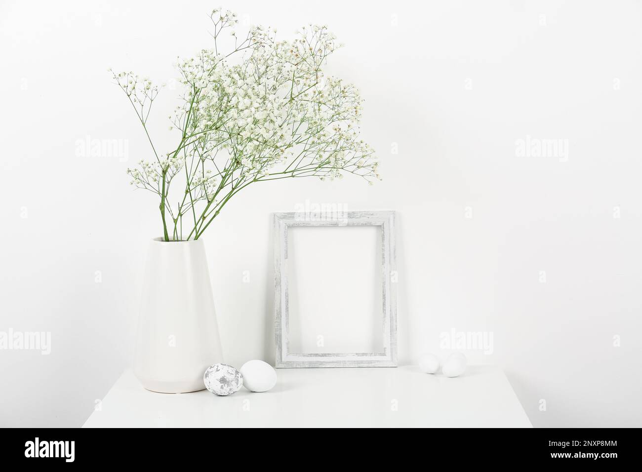 Blank frame, vase with gypsophila flowers and Easter eggs on white ...