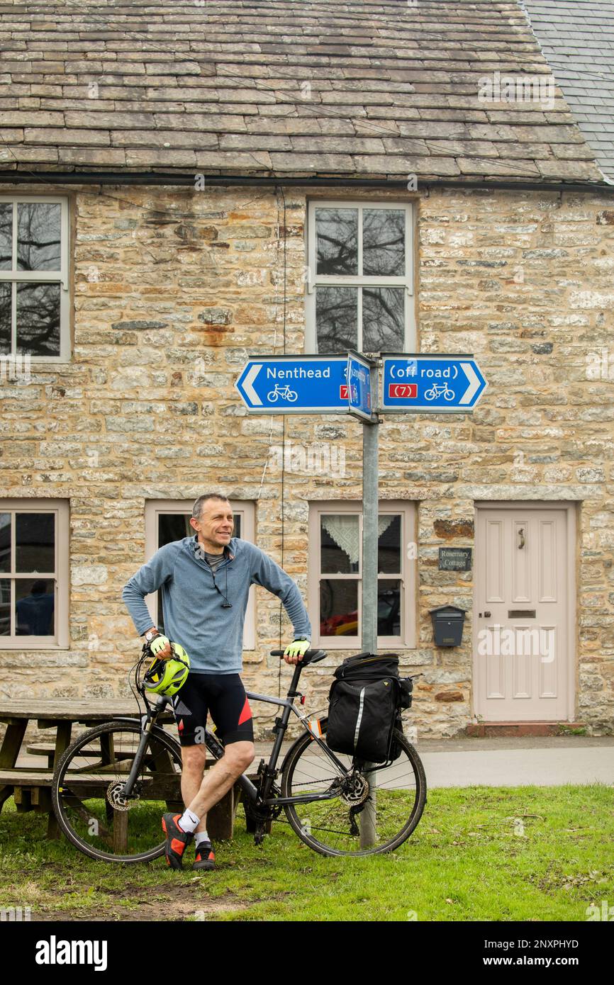 A cyclist with yellow helmet beneath a signpost for cycle routes to Nenthead, Langwathby and off road at Garrigill, Cumbria Stock Photo