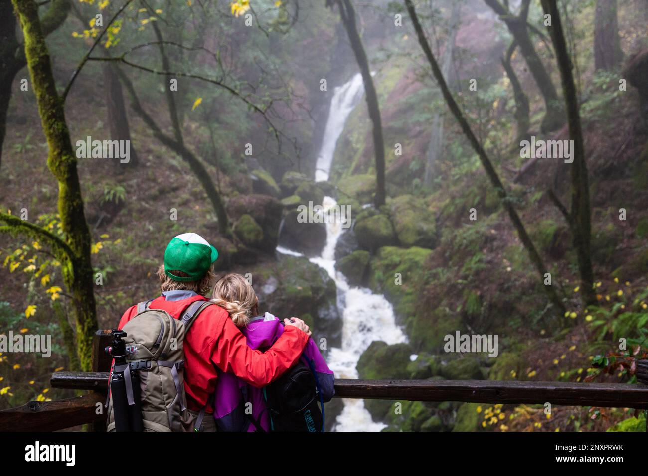 A man and woman pause while hiking to admire a waterfall on the Cataract Falls Trail in Golden Gate National Recreation Area, California. Stock Photo