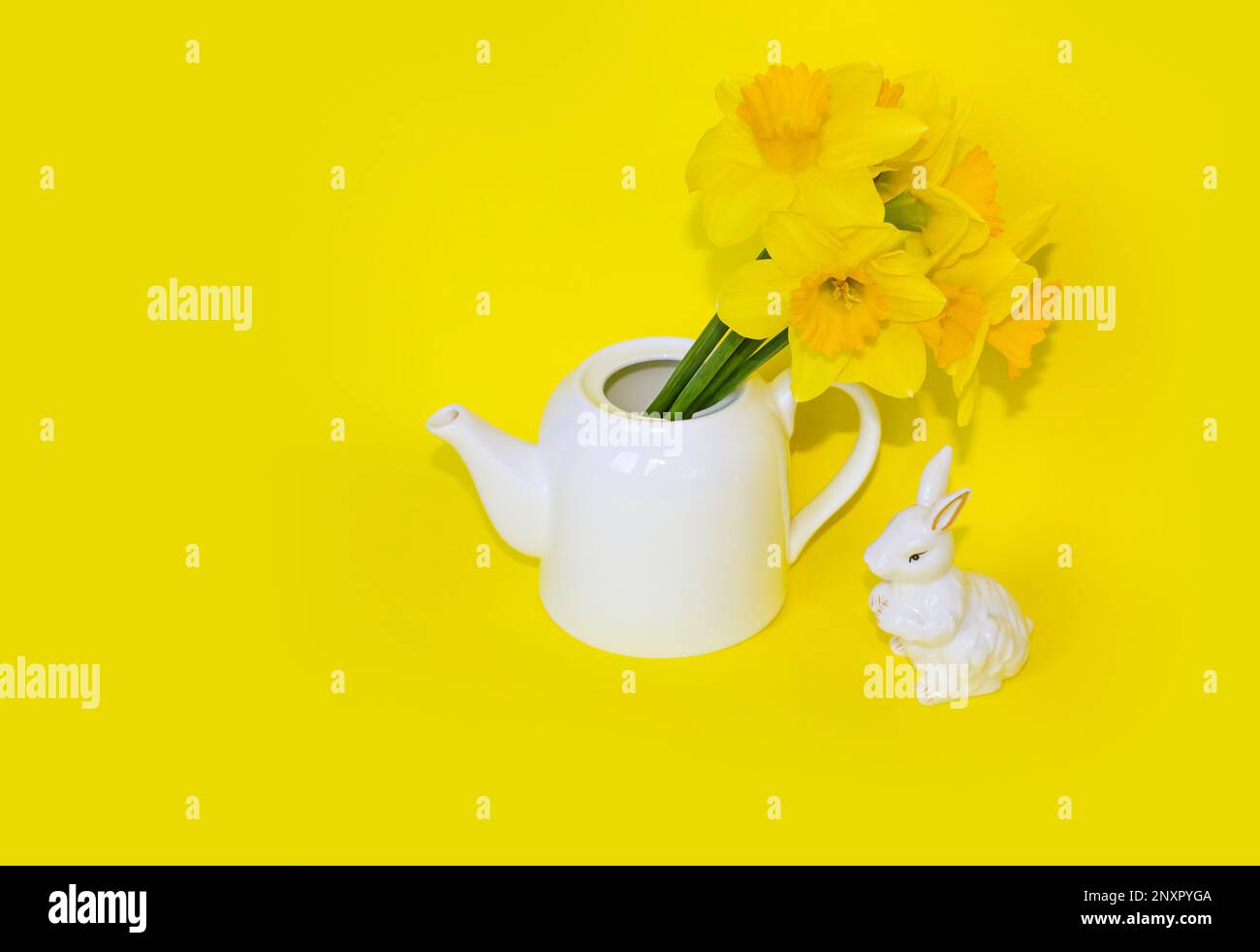 Jug with beautiful Daffodils and Easter bunny on yellow background with space for text. Home interior with easter decor. Daffodils in a vase, spring f Stock Photo