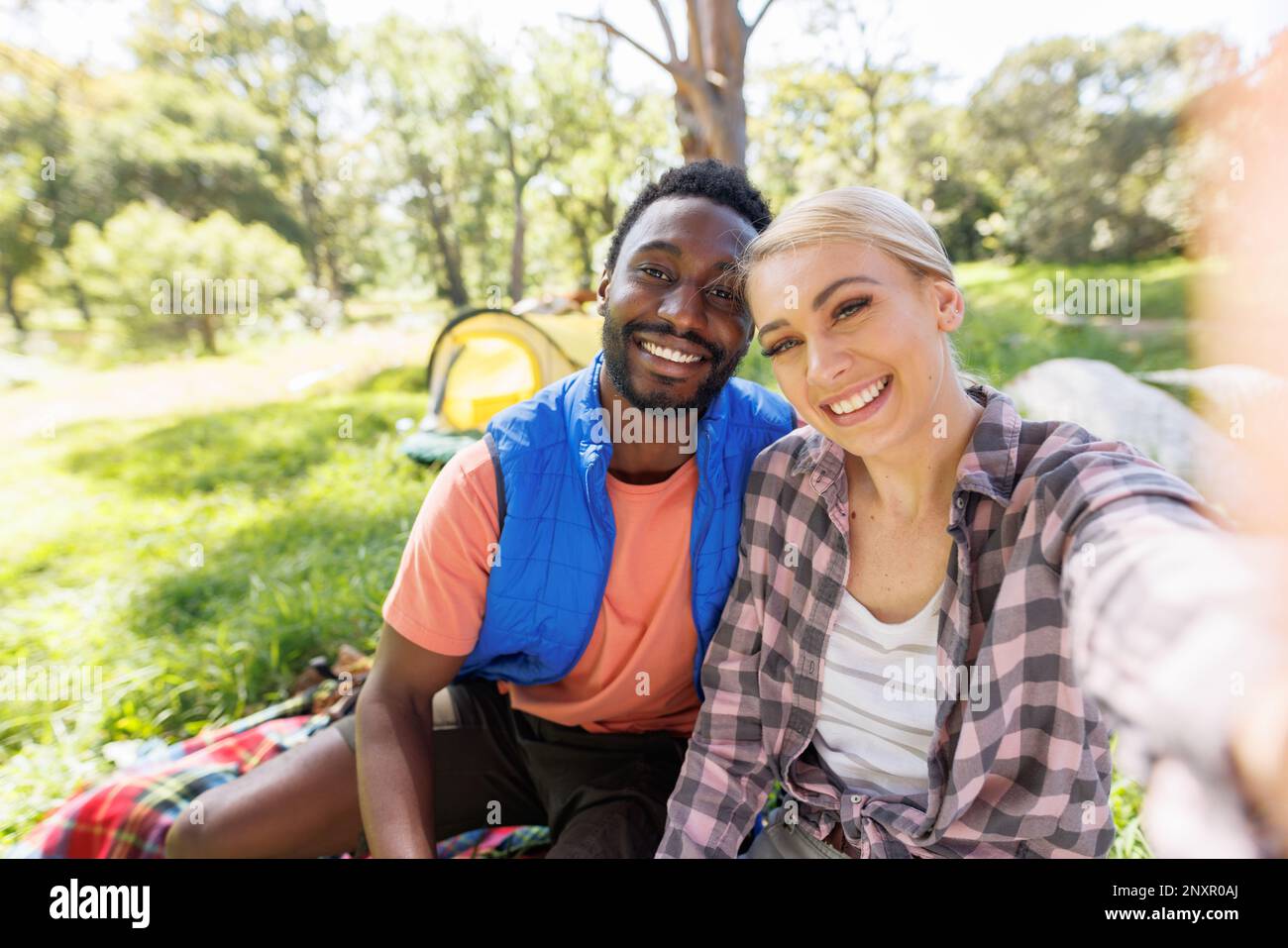 Happy, diverse couple on camping holiday smiling and taking selfie in countryside Stock Photo