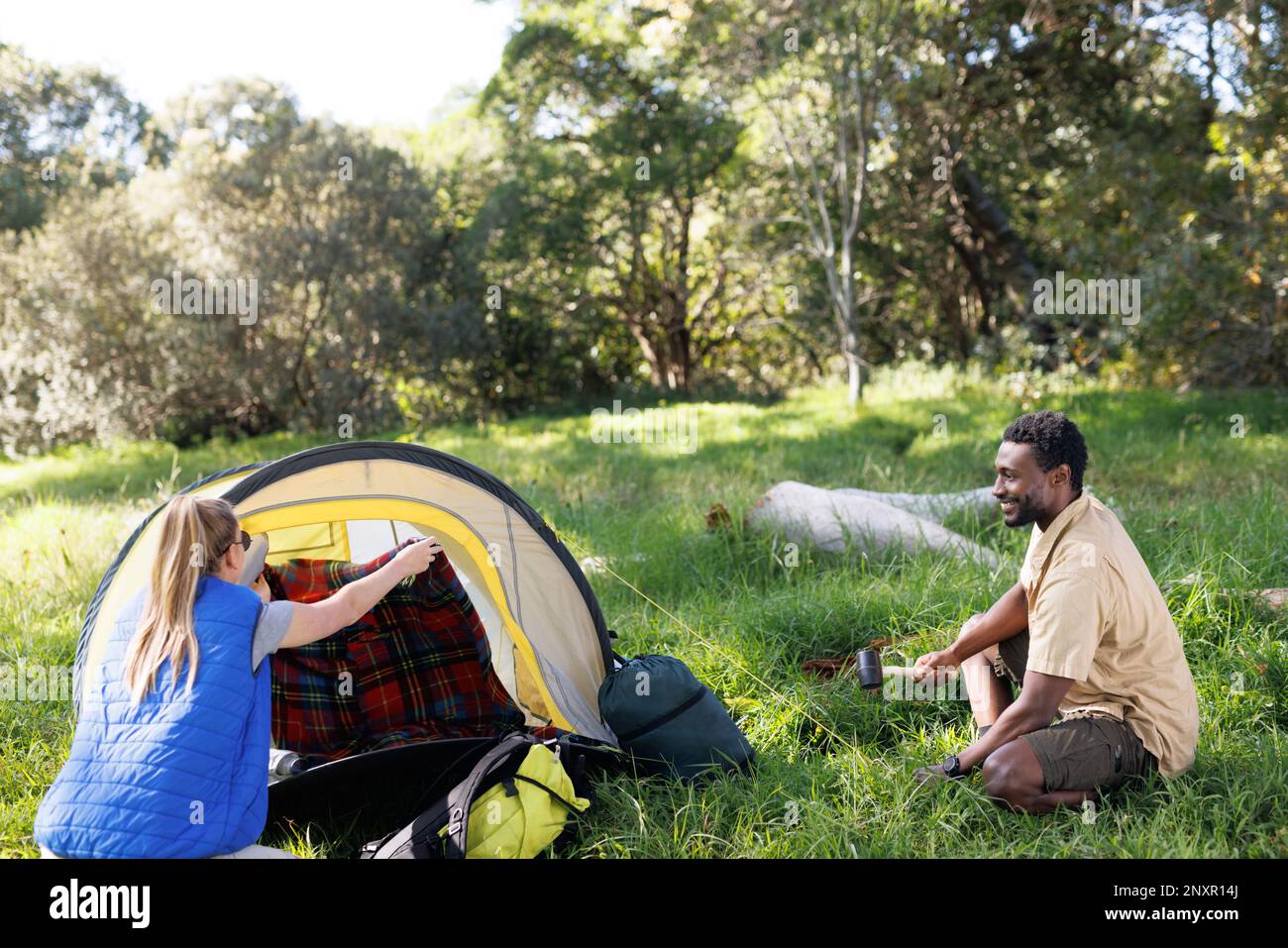 Happy, diverse couple camping in forest, pitching tent, setting up camp Stock Photo
