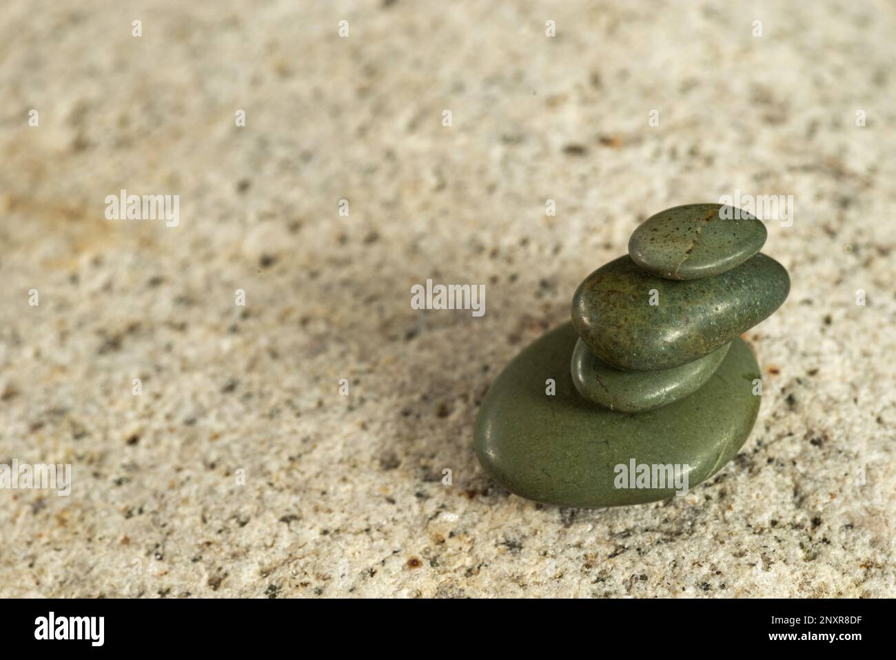 smooth stacked little jade pebbles stacked up on a much larger light granite cobble Stock Photo