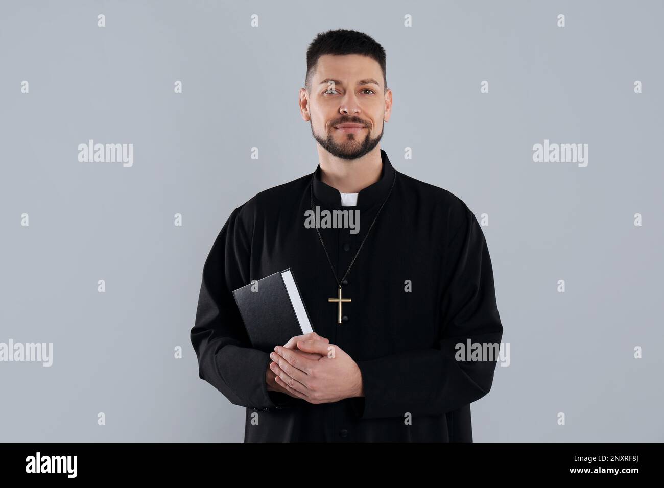Priest with Bible and cross on grey background Stock Photo
