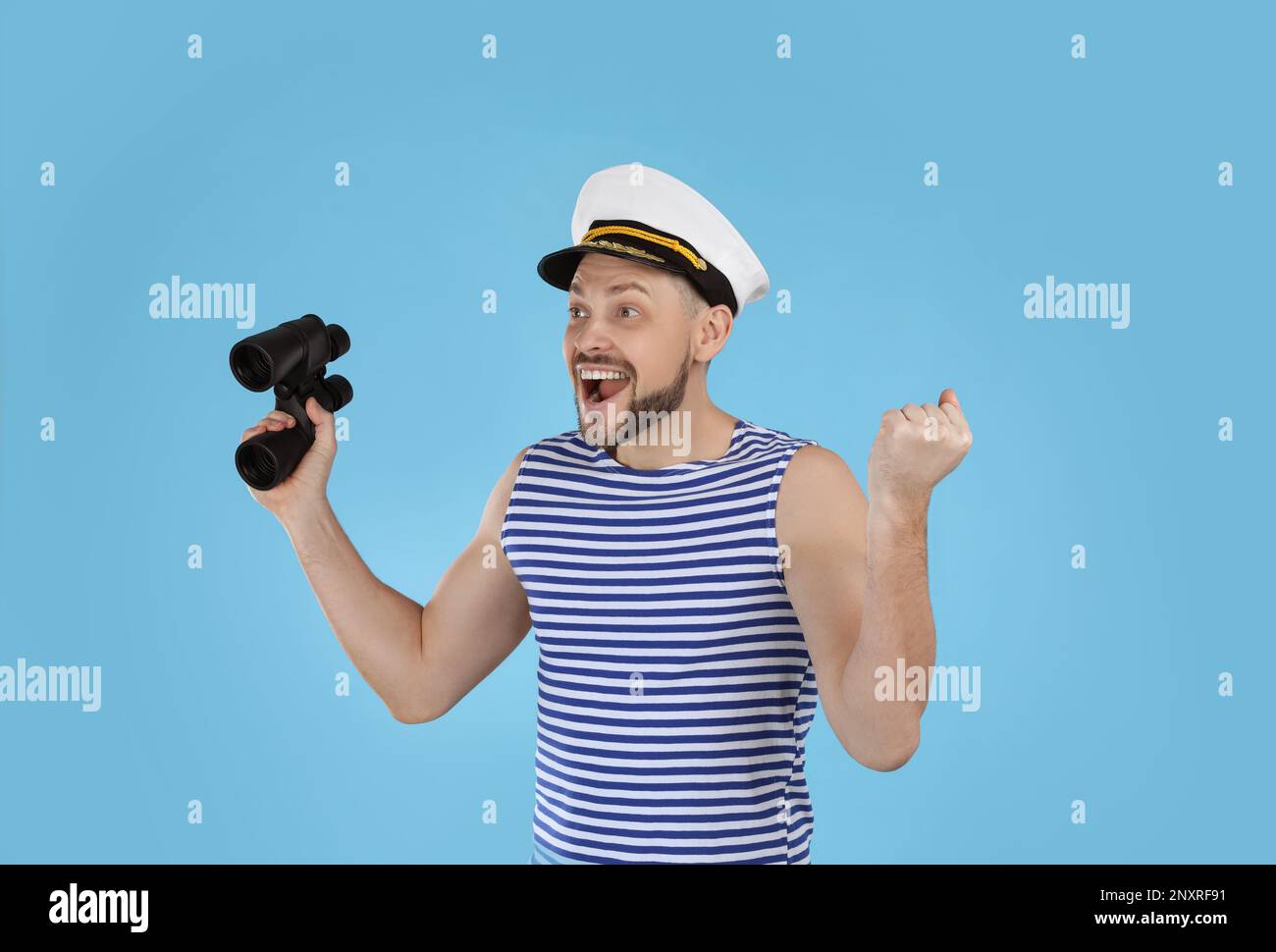 Happy sailor with binoculars on light blue background Stock Photo