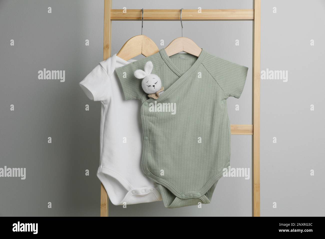Baby bodysuits hanging on ladder near light wall Stock Photo