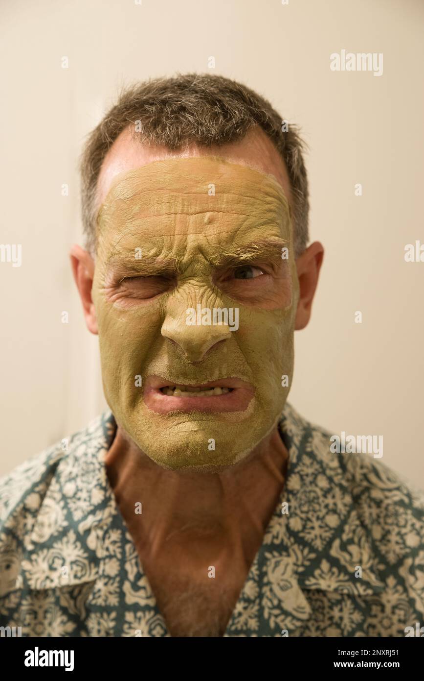 a middle aged man with a green clay facial mask makes an angry face Stock Photo