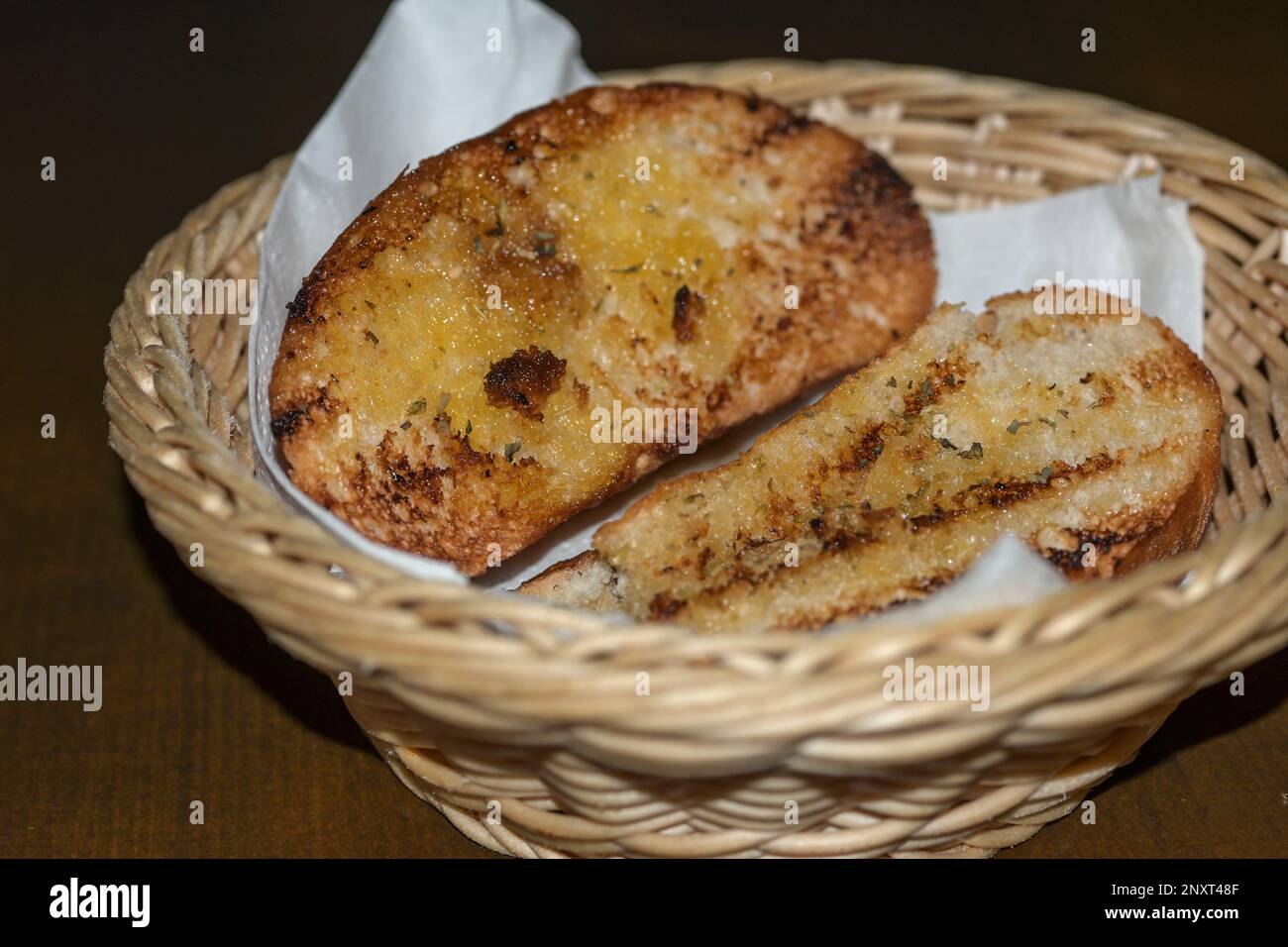 Bread slices roasted in olive oil with garlic and herbs, crunchy Mediterranean side dish in a small basket on a dark table, selected focus, narrow dep Stock Photo