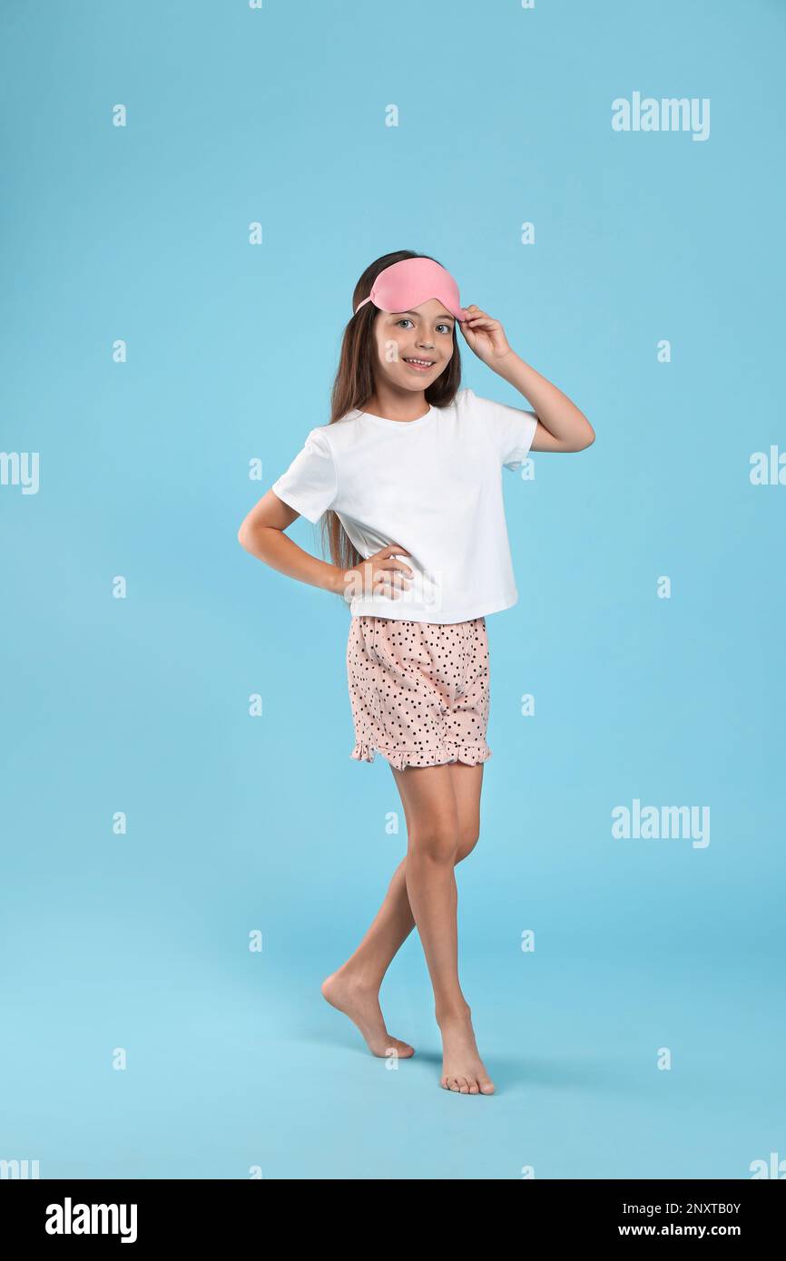 Cute girl wearing pajamas and sleeping mask on light blue background ...