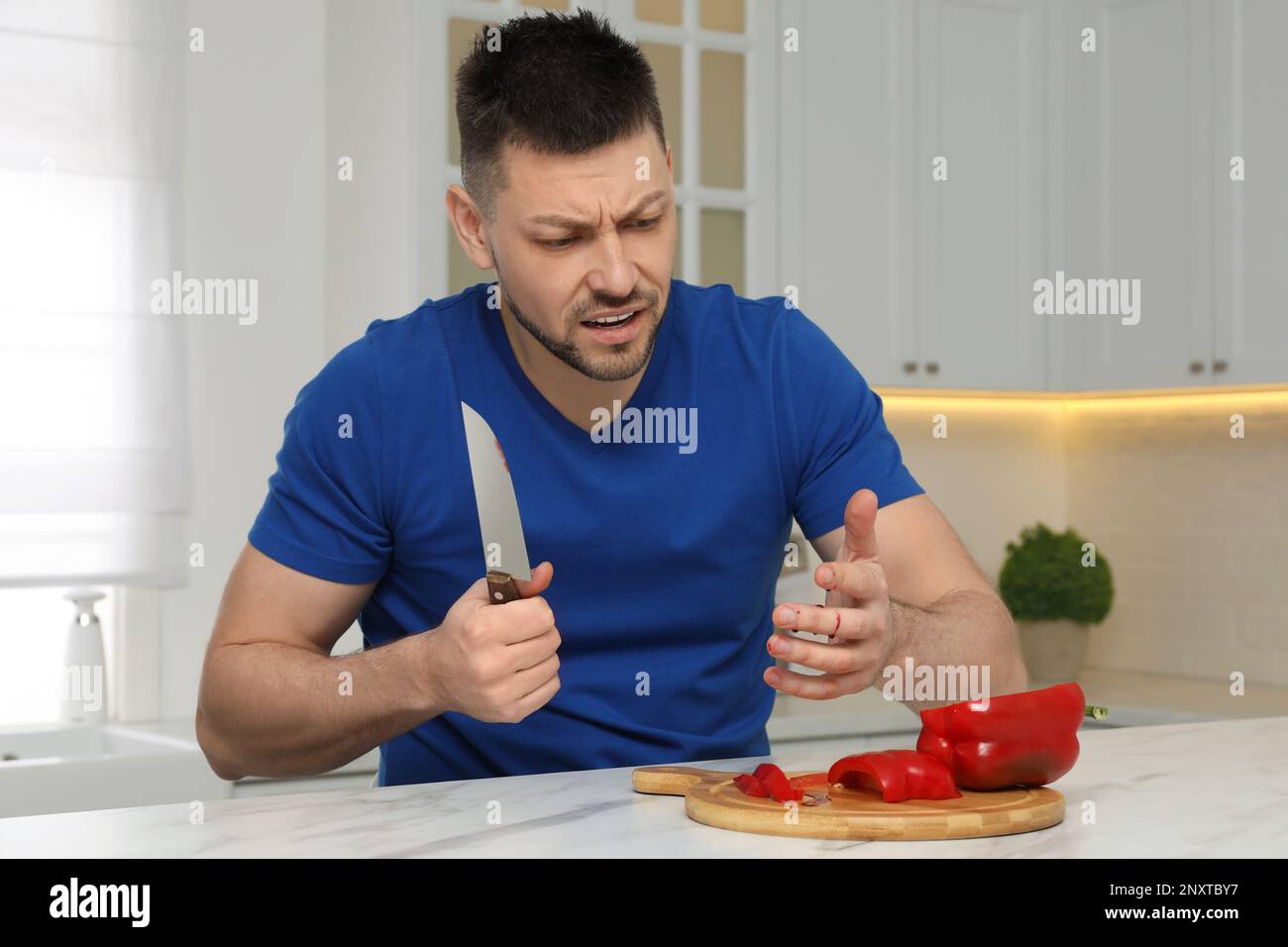 Man cut finger with knife while cooking at white marble table in