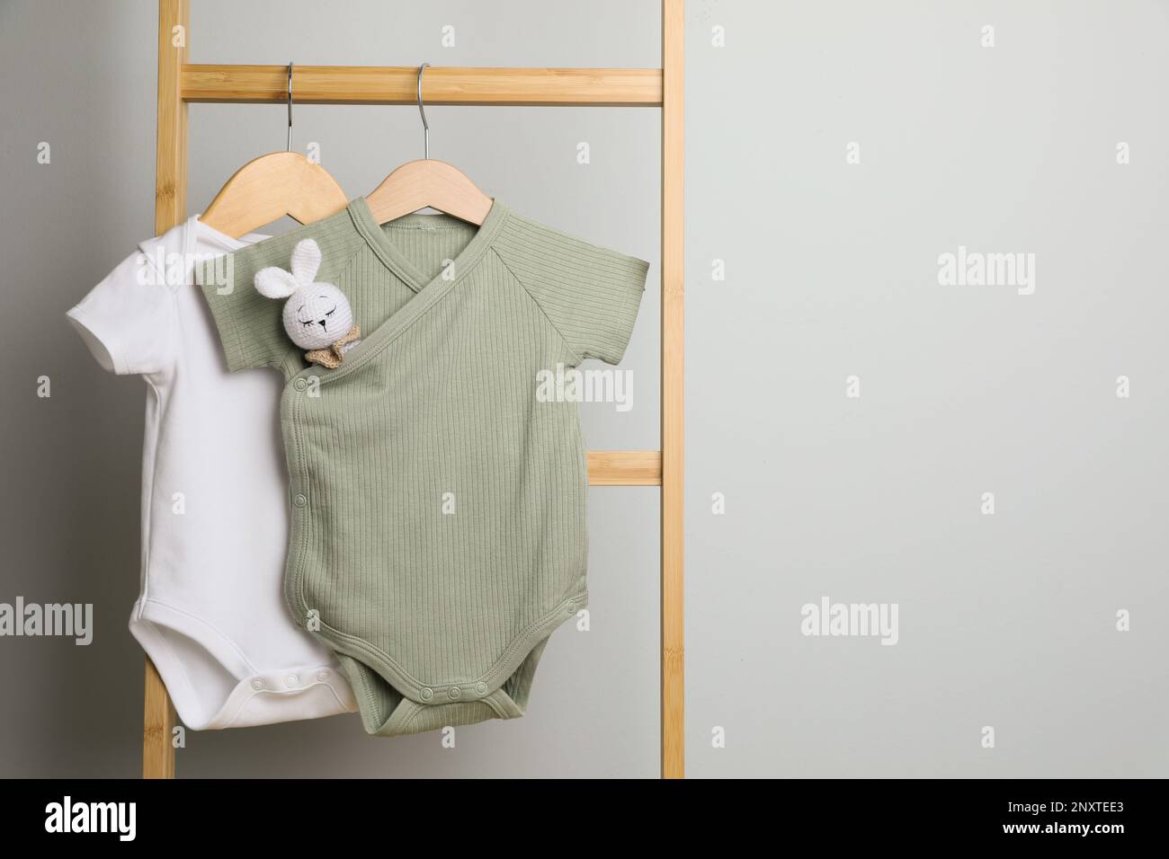 Baby bodysuits hanging on ladder near light wall, space for text Stock Photo