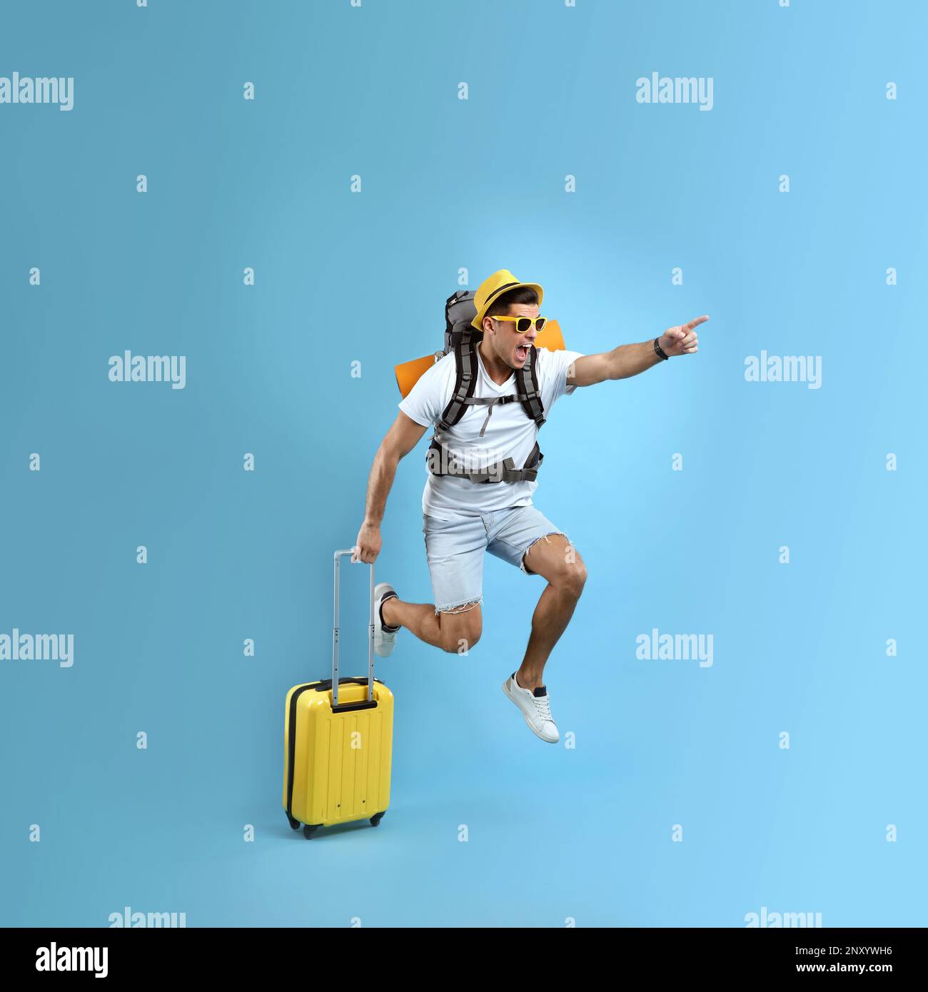 Emotional male tourist with travel backpack and suitcase jumping on turquoise background Stock