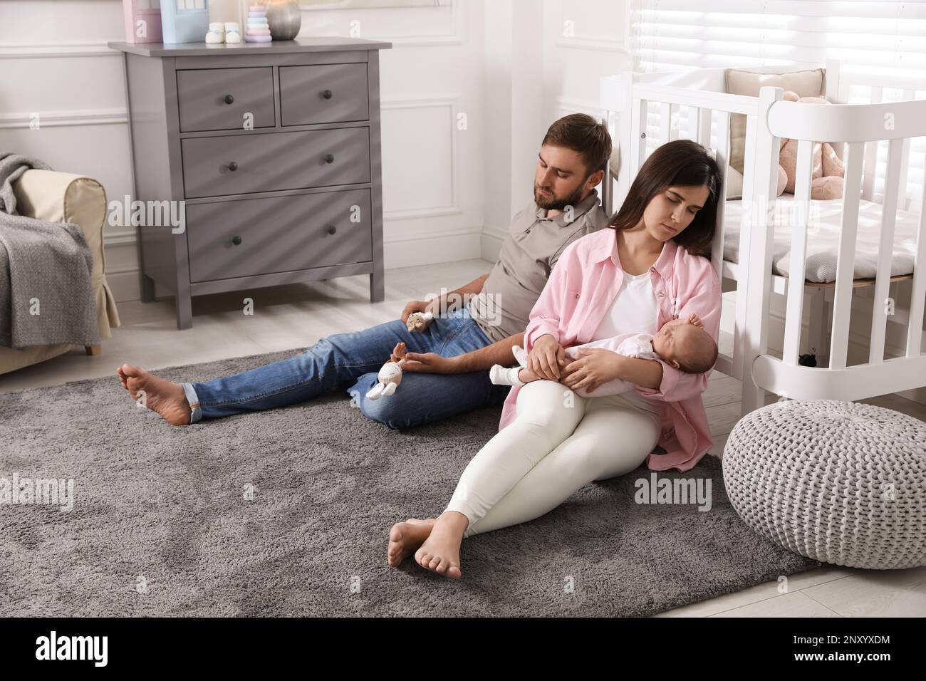 Tired young parents with their baby sleeping on floor in children's