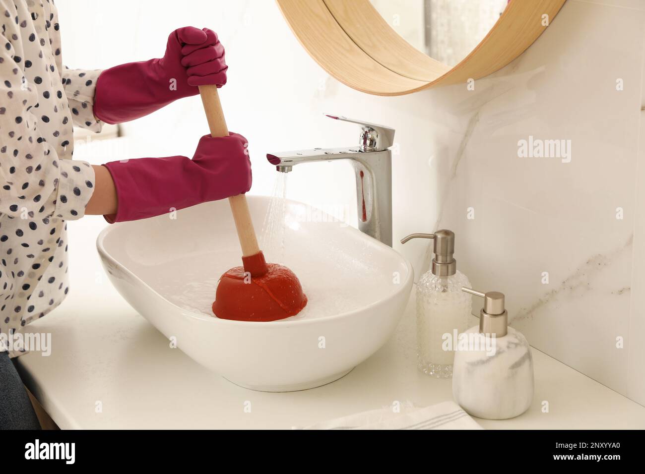 Woman using plunger to unclog sink drain in bathroom, closeup Stock