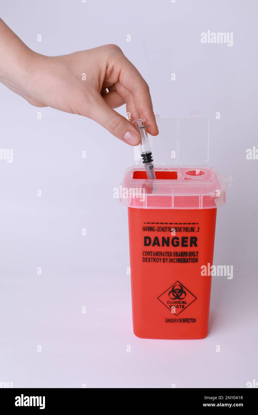 Woman throwing used syringe into sharps container on white background