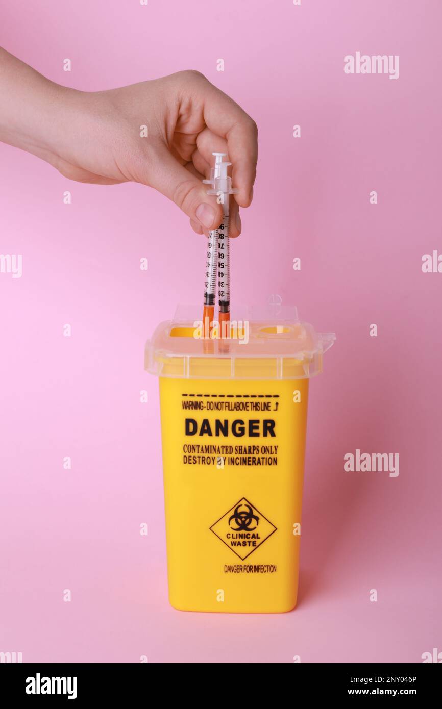 Woman throwing used syringes into sharps container on pink background