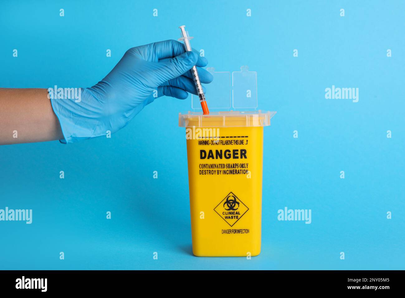 Doctor throwing used syringe into sharps container on light blue