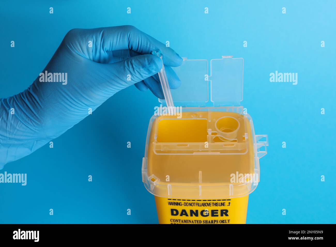 Doctor throwing used syringe needle into sharps container on light blue background, closeup