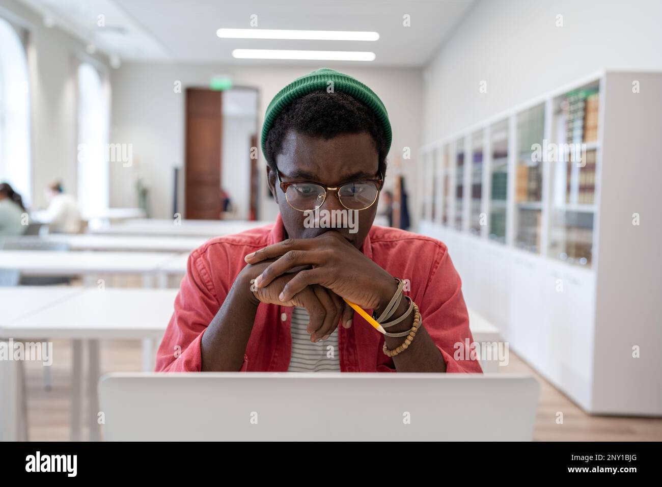 Thoughtful young African American man freelancer working remotely on laptop in public library Stock Photo