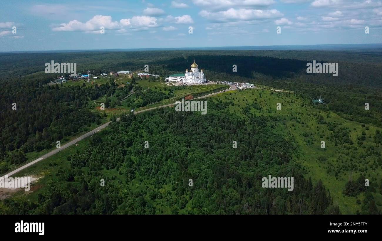 View from a height of a summer landscape with a forest and mountains. Clip. A green forest with spruces and a beautiful peasant temple in the middle s Stock Photo