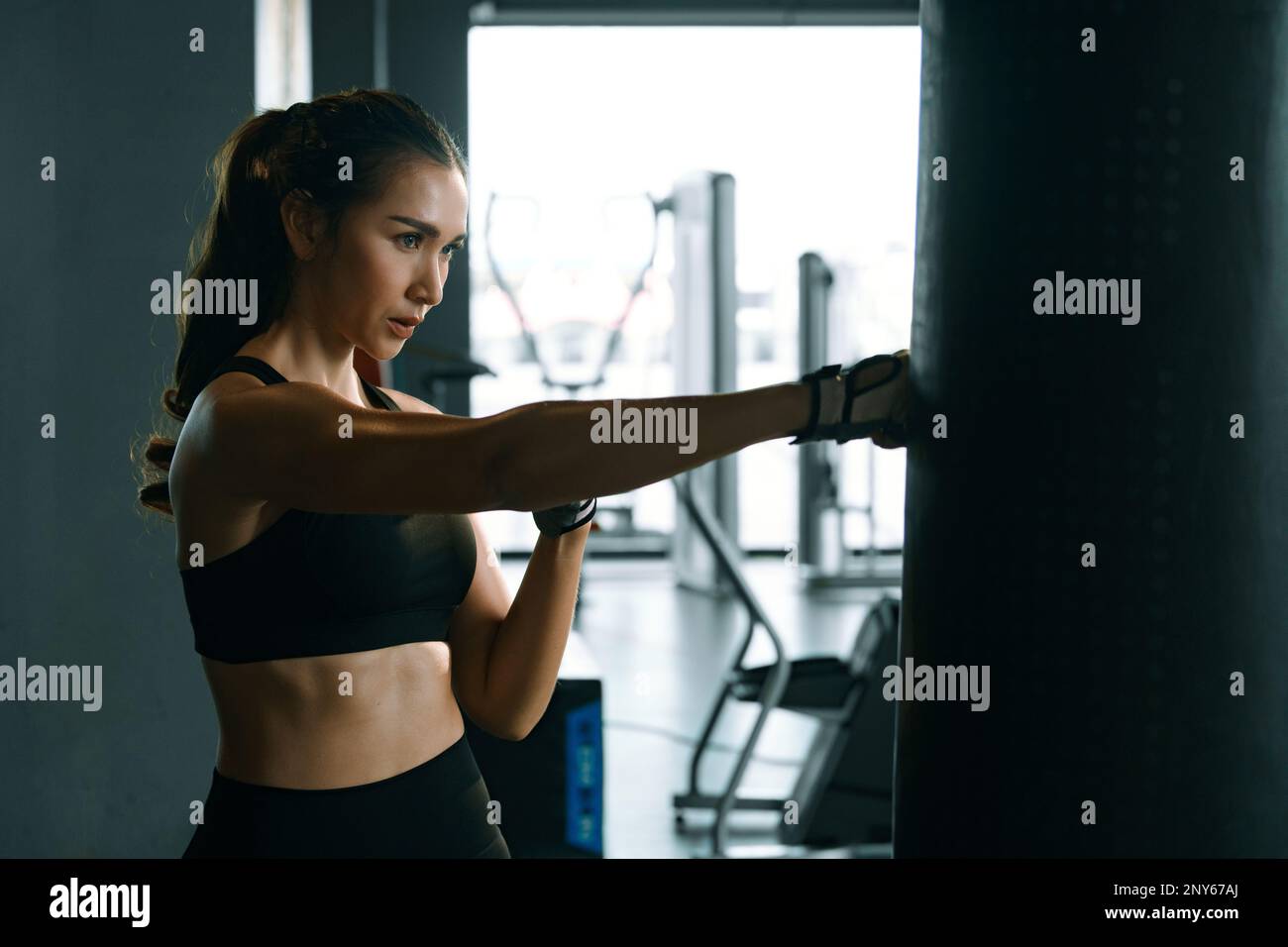 Young woman practicing boxing at the gym, she wears boxing gloves and hits a punching bag. Stock Photo