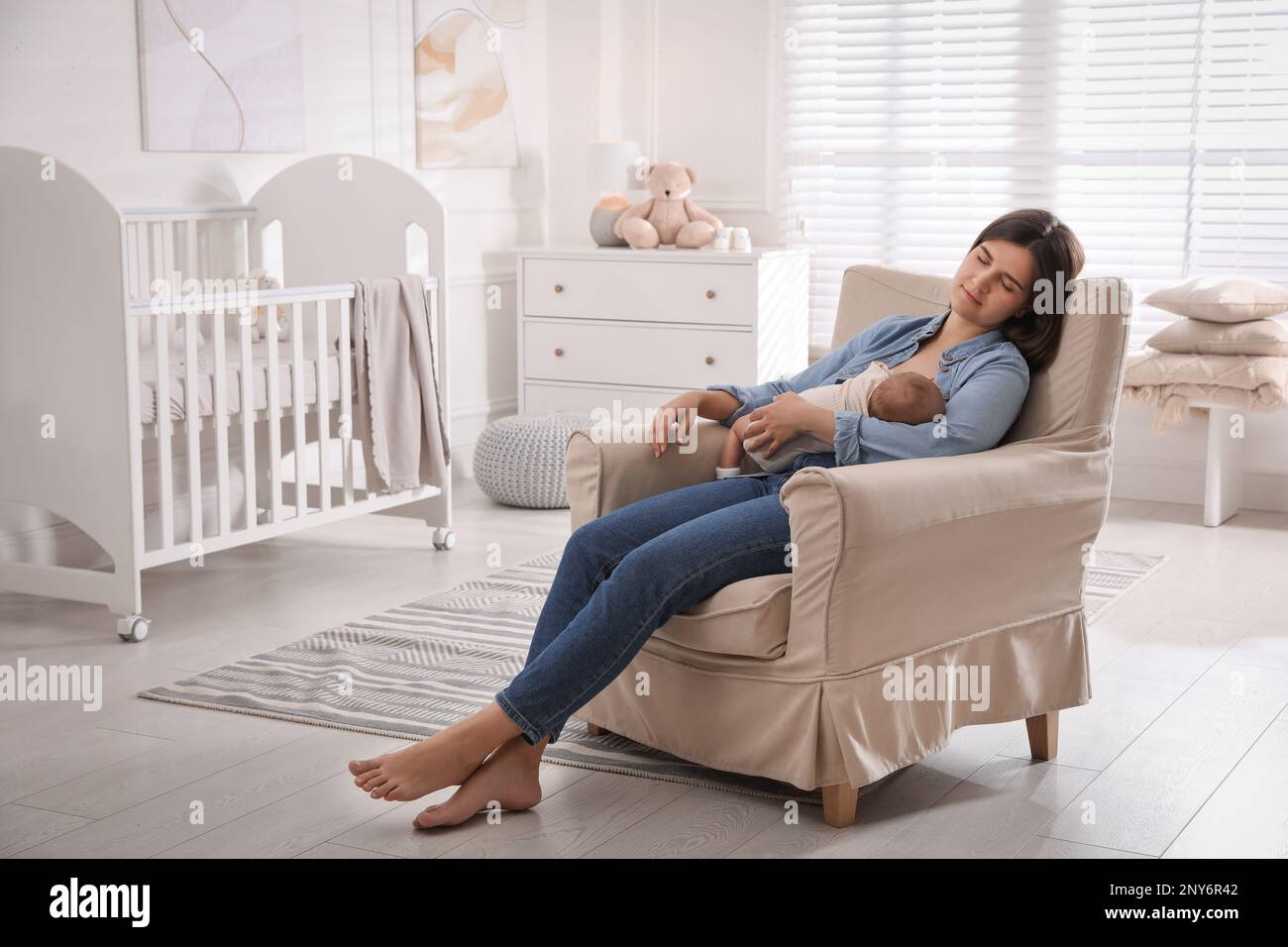 Tired young mother sleeping while breastfeeding her baby in children's
