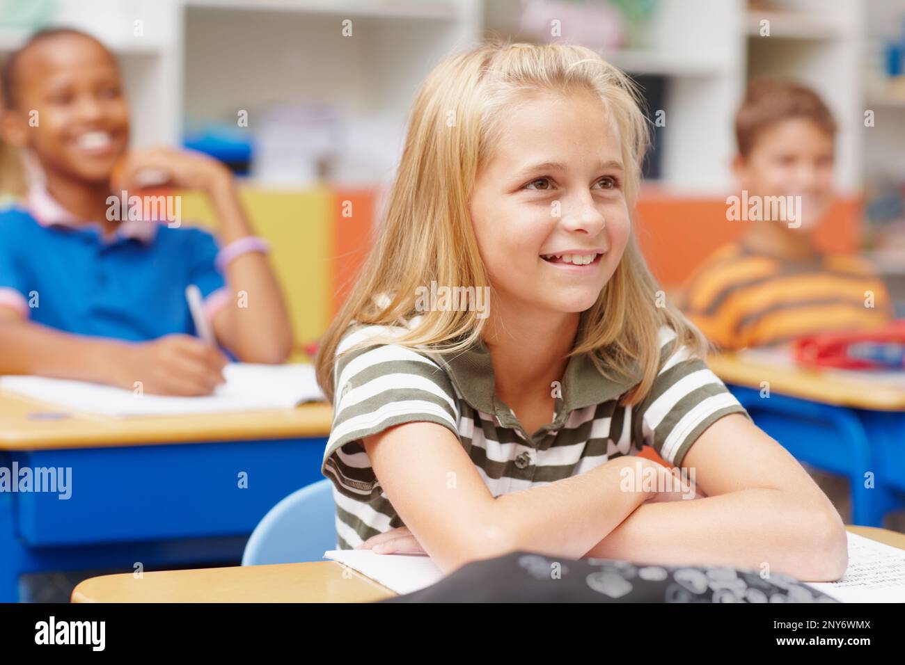 This school offers an inspiring education. Young blonde girl paying attention in class and smiling while enjoying a lesson- copyspace. Stock Photo