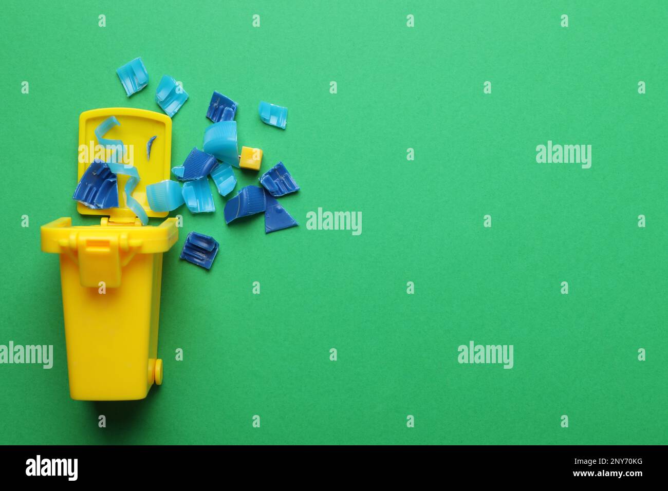 Mini recycling bin and broken plastic pieces on green background, flat