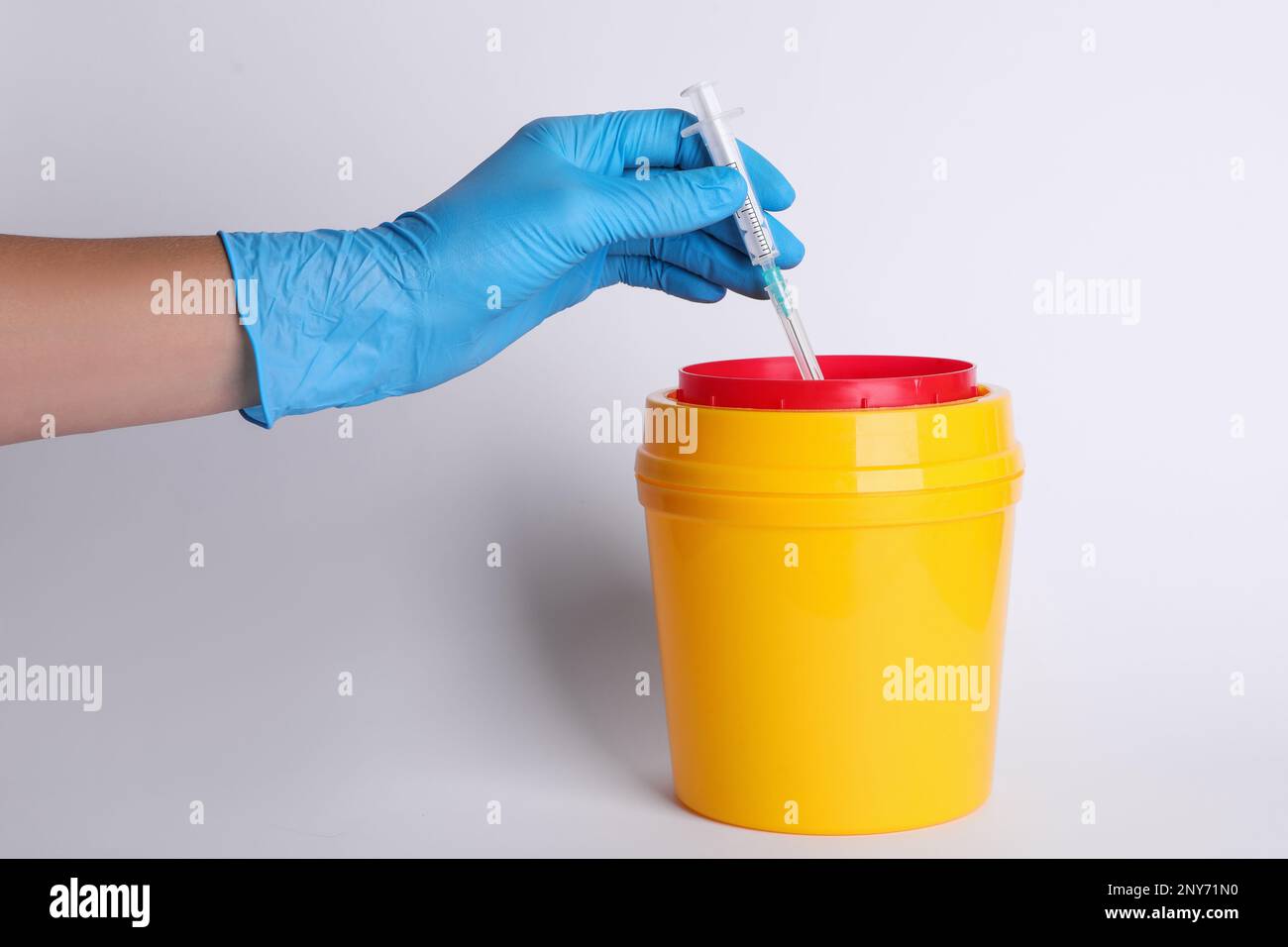 Doctor throwing used syringe into sharps container on white background