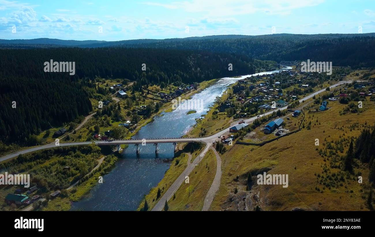 Aerial view of ecological place for living. Clip. Peaceful village with a river and bridge located surrounded by forest Stock Photo