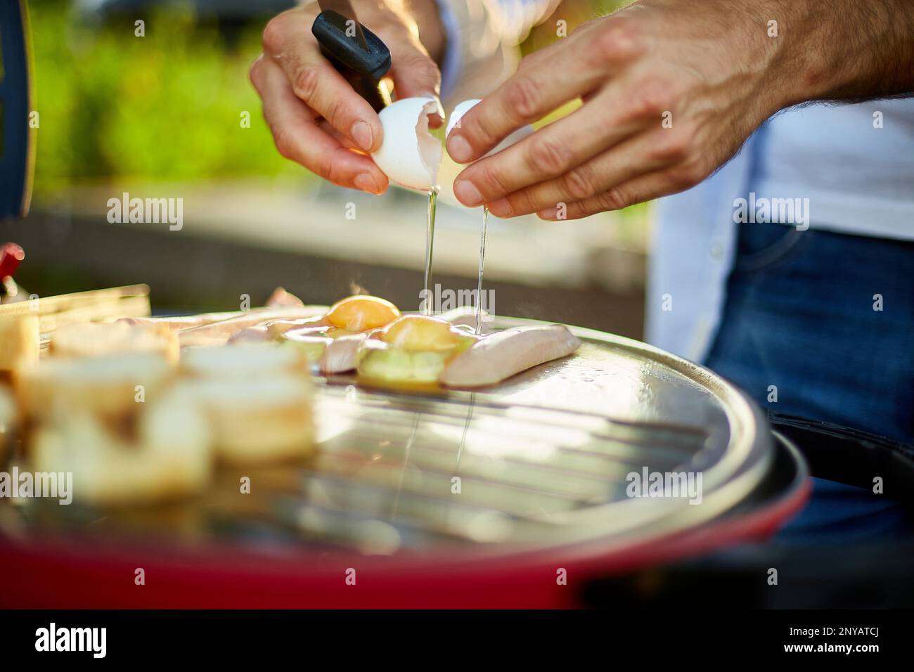 Close up on man's hand break eggs, roasting bruschetta and sausages, on the barbecue gas grill outdoor in the backyard, Breakfast On Grill, summer Stock Photo