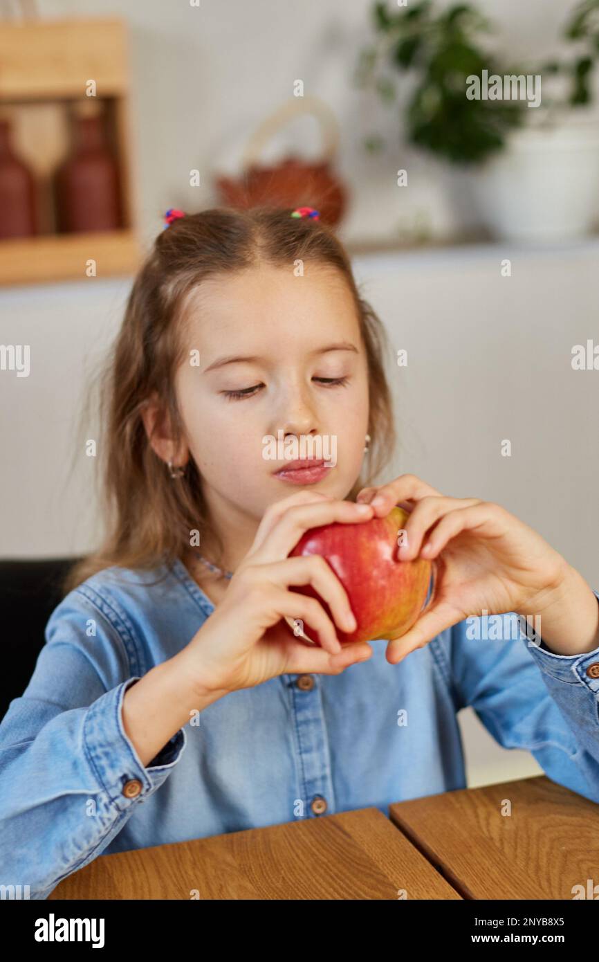Cute little girl eat red apple at home at kitchen interior, yummy