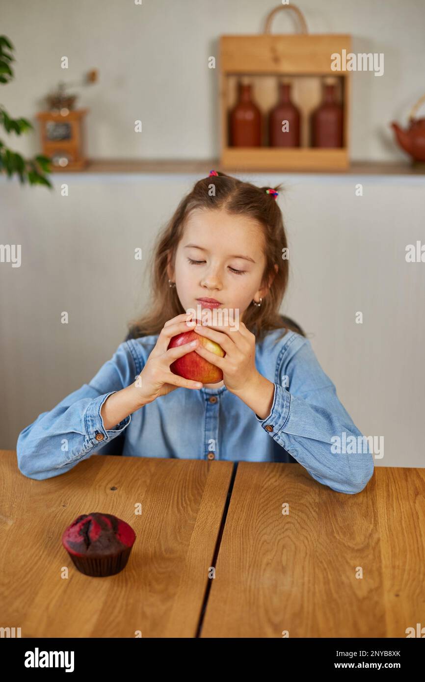 Cute little girl eat red apple at home at kitchen interior, yummy