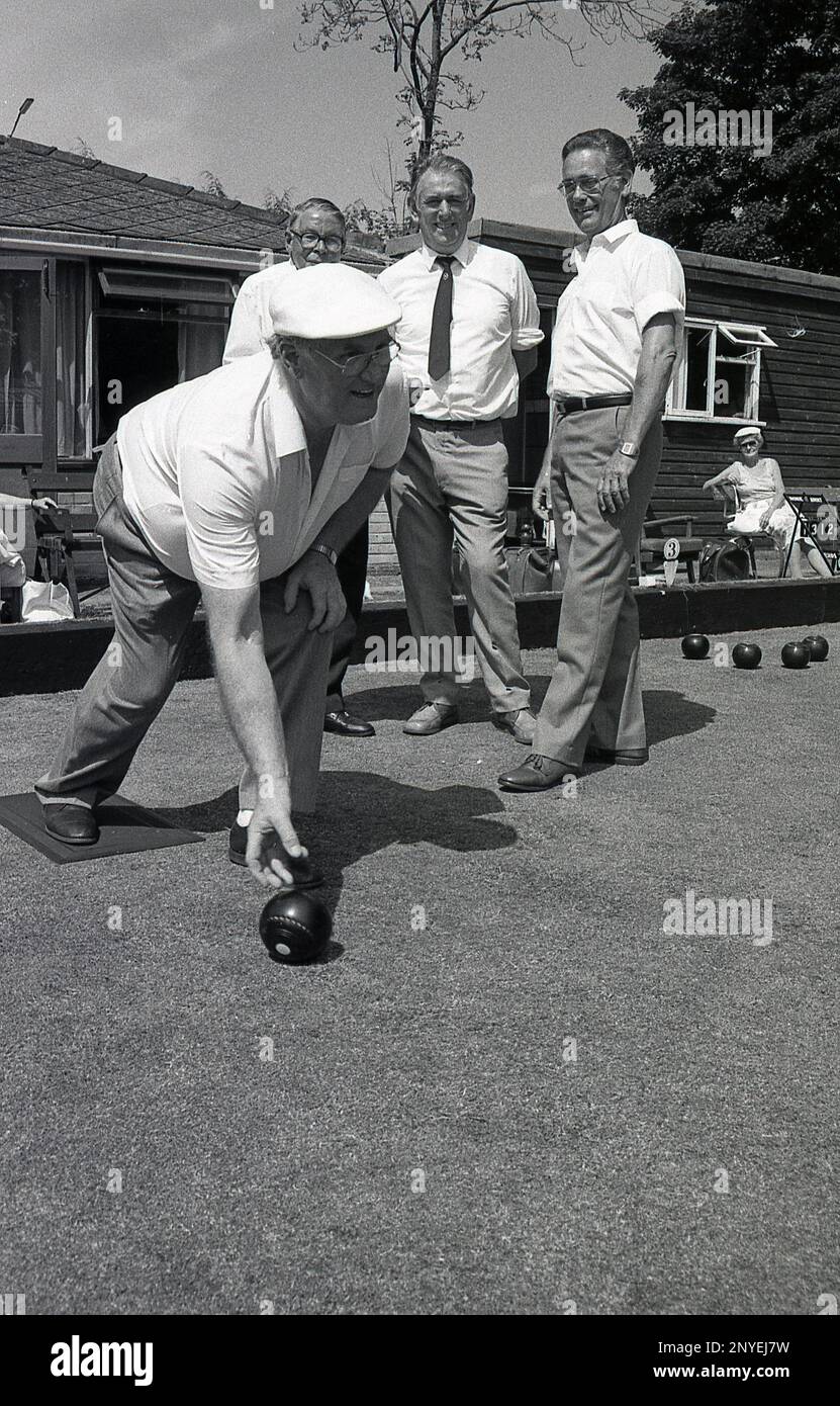 1989, historical, lawn bowls, outside a clubhouse, three men watch another man rolling a ball on a bowling green, England, UK. Stock Photo