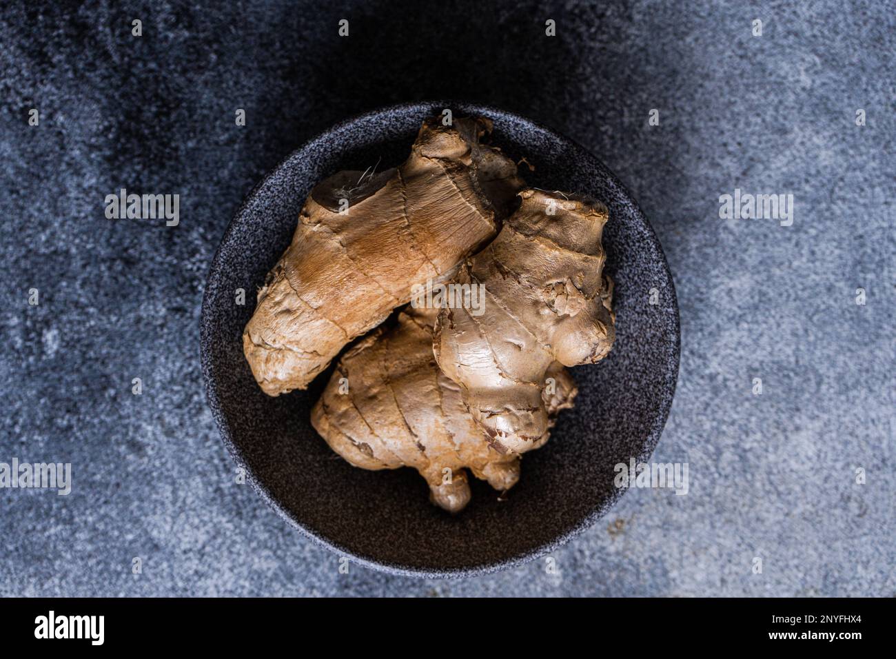 Black stone bowl with ginger roots on concrete kitchen table Stock Photo