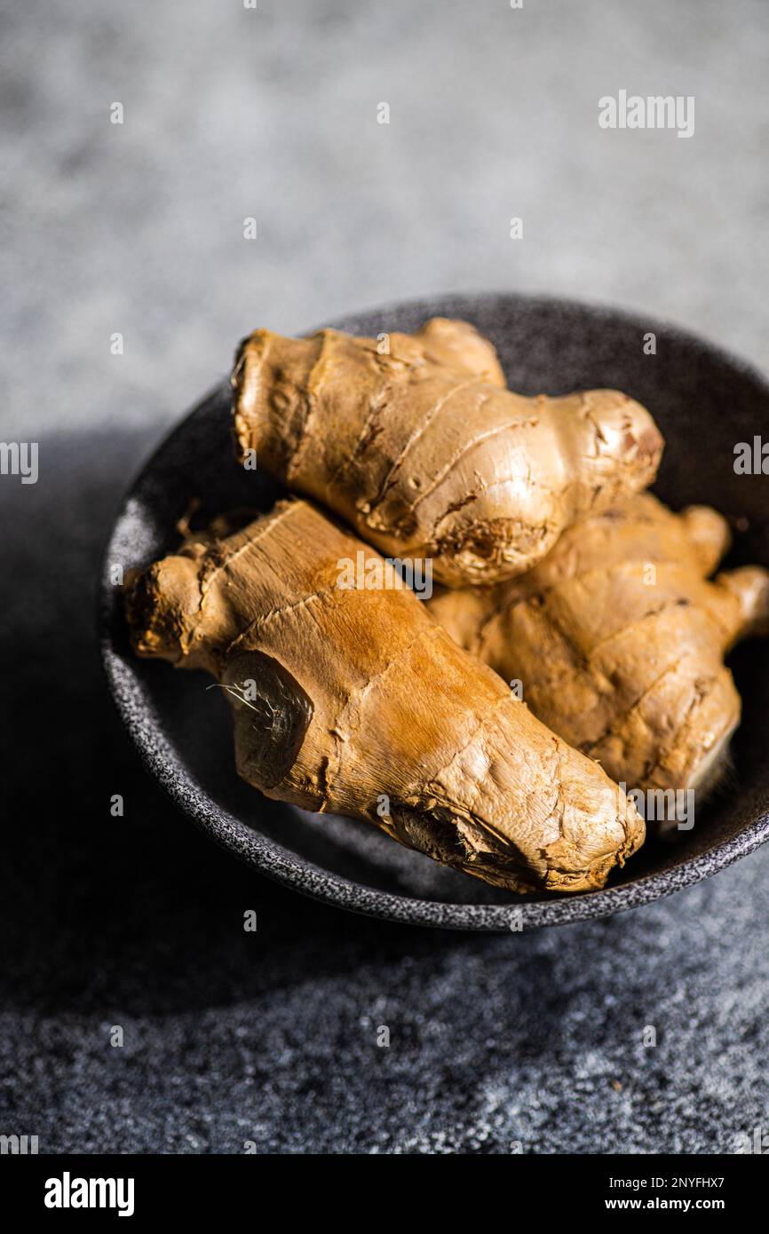 Black stone bowl with ginger roots on concrete kitchen table Stock Photo