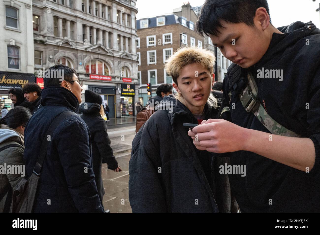 Two Asian males use a mobile/cell phone for information in city setting. London UK Stock Photo