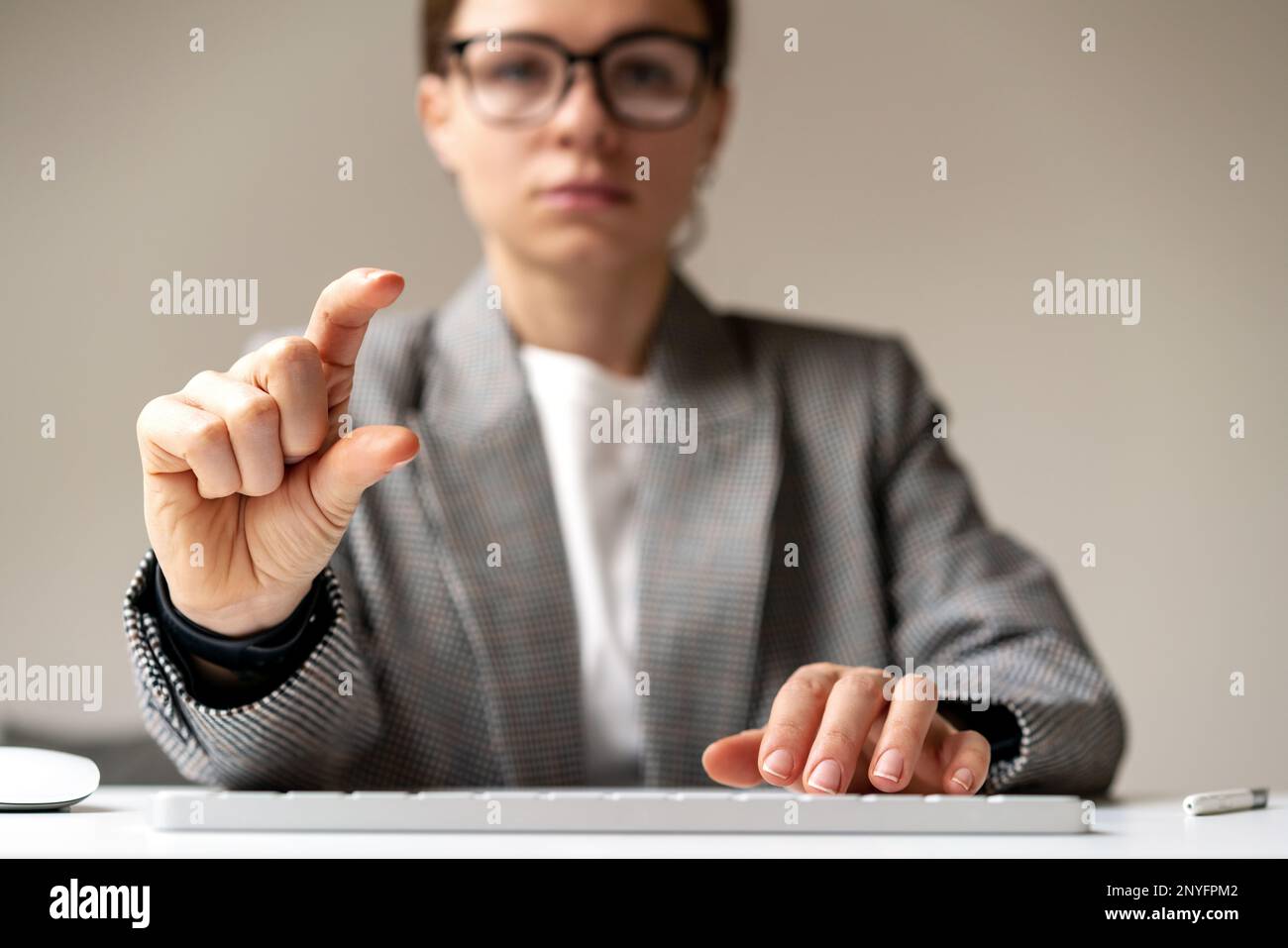 Front view woman sitting at desk using computer keyboard and holding virtual object between her fingers. Stock Photo