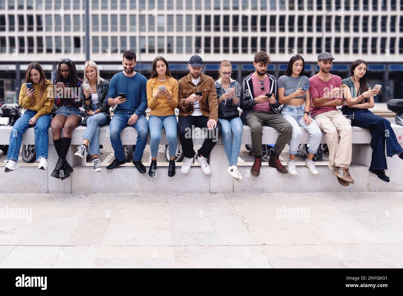 A group of eleven teenagers sitting on a wall, all with their heads